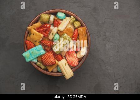 Primo piano di cracker di riso giapponesi in una ciotola con sfondo isolato. Cracker di riso colorati assortiti su sfondo nero. Spuntini per feste. Foto Stock