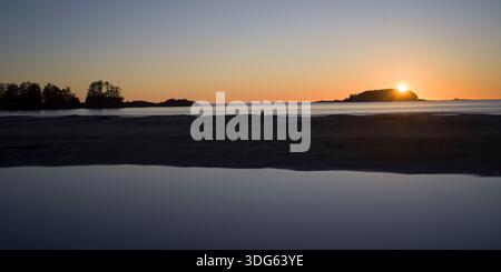 Tramonto su un oceano calmo con la silhouette di alberi e isole all'orizzonte. Tofino, Columbia Britannica, Canada Foto Stock