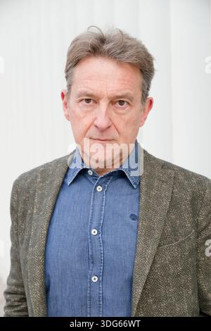 Uomo con giacca in tweed e camicia in denim si staglia su una parete bianca con un'espressione seria. Italia Foto Stock