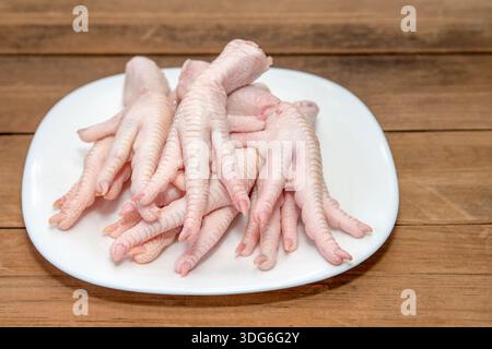 Piedi di pollo pronti per preparare il brodo di collagene su un tavolo rustico di legno. Piedini di pollo crudi posizionati su un piatto su un tavolo di legno, per preparare il collagene-R. Foto Stock