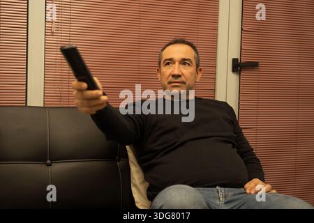 Uomo che si rilassa su un divano, tiene in mano un telecomando e si diverte a divertirsi Foto Stock