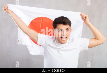 Lo spettatore maschio attivo e pieno di energia tiene in mano la bandiera nazionale del Giappone e canta slogan popolare. Foto Stock