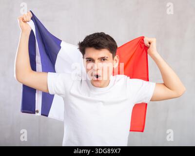 Eccitato, attivo spettatore maschile detiene bandiera nazionale della Francia in mani e canti slogan popolare Foto Stock