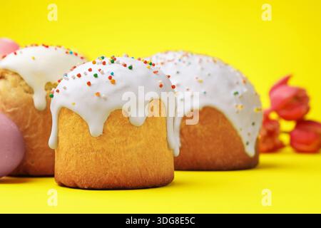 Deliziose torte di Pasqua e tulipani su sfondo giallo, primo piano Foto Stock
