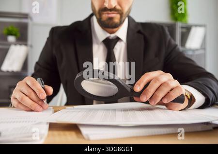 Primo piano di un uomo d'affari che controlla i documenti e rivede i dati con una lente di ingrandimento Foto Stock