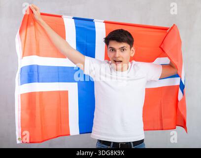 Il giovane dipendente detiene la grande bandiera nazionale della Norvegia con un sorriso sicuro che mostra i denti. Foto Stock