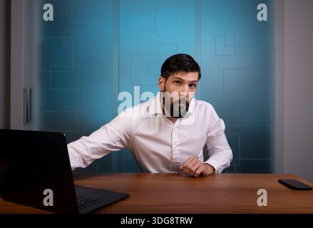 Uomo seduto in un ufficio moderno che rappresenta un'azienda o un'azienda con indosso una camicia bianca Foto Stock