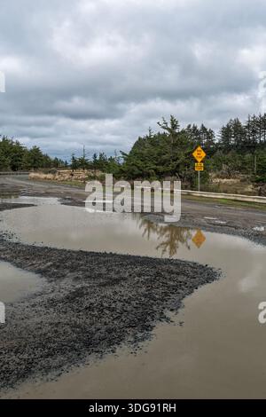 Un segnale stradale che segnala l'allagamento si riflette su una strada allagata Foto Stock