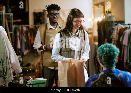 Giovane donna che acquista abbigliamento di seconda mano da Shop Assistant indoor Foto Stock
