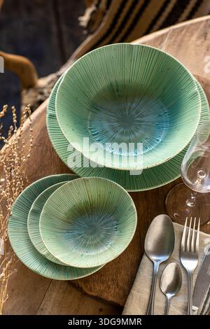 Una vista dall'alto verso il basso di un sofisticato tavolo con piatti e ciotole in ceramica verde smeraldo con una texture radiale unica al sole. Il set è AC Foto Stock