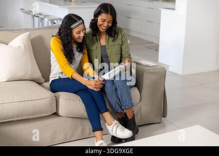 Mamma e figlia adolescente diverse leggono i contenuti delle buste sul divano beige nel soggiorno Foto Stock