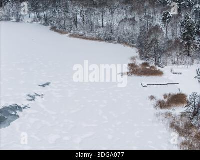 Vista aerea di un tranquillo lago Galve coperto di neve con il bordo scuro e strutturato della foresta che contrasta con l'ampio bianco di Trakai, Lituania. Foto Stock