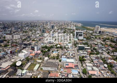 Vista aerea di edifici e strade che si estendono fino alla costa, dove l'oceano incontra il cielo in un paesaggio urbano denso, Lagos, Nigeria. Foto Stock