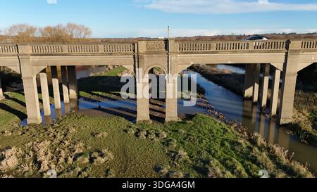 Veduta aerea di un ponte di cemento che si estende sul tranquillo fiume, con i suoi archi che gettano lunghe ombre sulle rive erbose sottostanti, Wellingborough, Engl Foto Stock