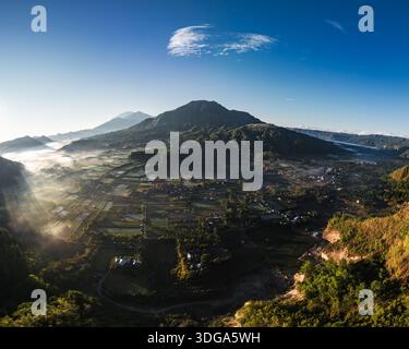 Vista aerea di una maestosa catena montuosa velata in eterea nebbia, le sue vette baciate dalla luce dorata dell'alba, Bali, Indonesia. Foto Stock