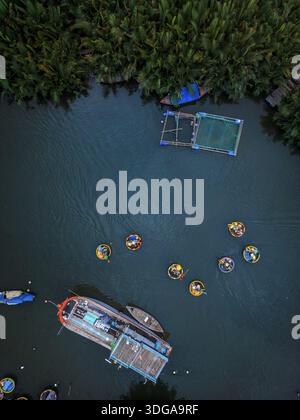 Vista aerea delle barche a cesto che punteggiano le acque tranquille vicino a una vegetazione lussureggiante, catturando l'essenza della vita lungo il fiume, Quảng An, Thành phố Hội Nam, Vietna Foto Stock