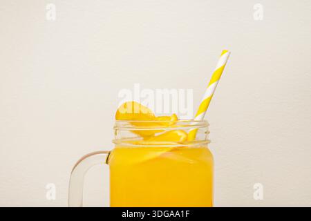Una caraffa cilindrica di vetro alta, mezza riempita con un vivace frullato di mango arancio e frutto della passione, che vanta una consistenza cremosa senza frutta visibile Foto Stock