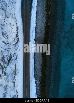 Vista aerea di un netto contrasto tra il terreno innevato e la costa rocciosa scura che incontra il mare turchese, Kvaløya, Troms, Norvège. Foto Stock