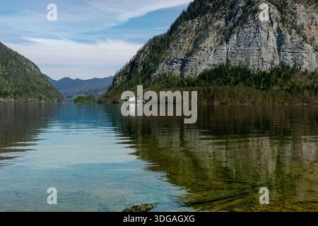Hallstatt, Austria. Tranquillo lago alpino circondato da ripide catene montuose che si riflettono in acque turchesi cristalline. Piccolo insediamento visibile sulla costa. Foto Stock