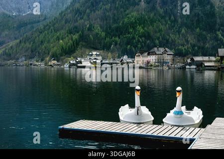 Hallstatt, Austria. Pedalò a forma di Swanshape attraccate al molo di legno sullo splendido lago alpino. Villaggio storico incastonato tra montagne e foreste Foto Stock