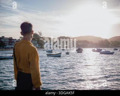 L'uomo visto da dietro guardando le barche del porto durante l'ora d'oro, lo stile di vita dei viaggi costieri Foto Stock