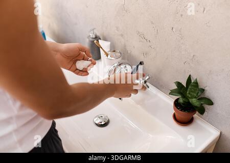 In un ambiente accogliente, un giovane si concentra sul lavarsi le mani, irradiando tranquillità e calore. Foto Stock