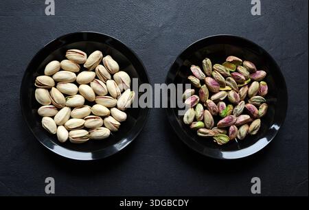 Due ciotole nere di pistacchi, a sinistra con il guscio e a destra con i pistacchi sgusciati isolati su sfondo nero. Cibo secco sano e vegetariano. Foto Stock