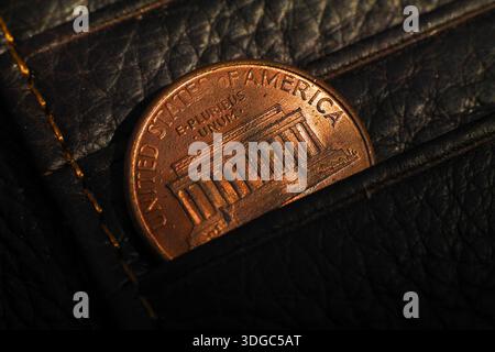 Un primo piano di un penny americano di rame incastrato in un portafoglio nero in pelle, che simboleggia risparmi personali, budget e gestione finanziaria. Foto Stock