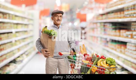 Uomo anziano che fa acquisti di generi alimentari in un supermercato con carrello e sacchetto di carta Foto Stock