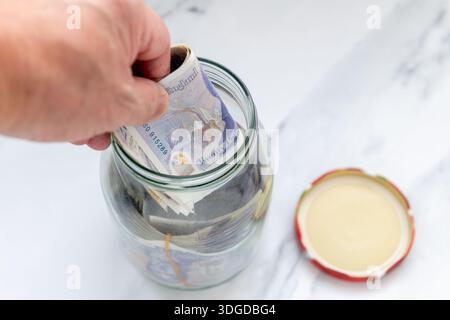 Una persona che mette banconote in un vaso di vetro. Foto Stock