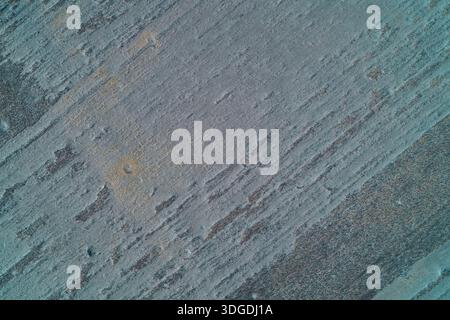 Un'esposizione astratta di texture graffiate e intemperie in tonalità blu-grigio, che ricordano il cemento armato o il metallo usurato. Questa cattura aerea di una superficie ghiacciata fornisce uno sfondo grunge naturale ad alta risoluzione adatto per progetti industriali o di dimensioni minime Foto Stock