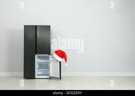Frigorifero con cappello di Babbo Natale rosso sulla porta aperta in camera. Spazio per il testo Foto Stock