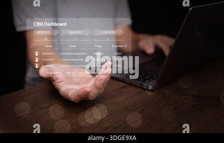 Uomo d'affari che utilizza un computer portatile con interfaccia dashboard CRM che galleggia sopra la mano. Concetto di gestione digitale delle relazioni con i clienti, generazione di lead, softw Foto Stock