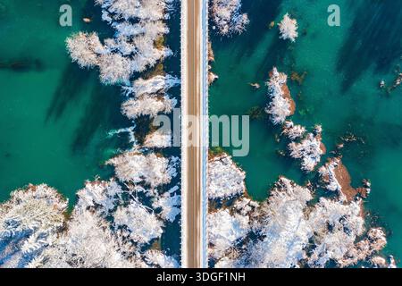 Ponte in legno sul fiume Mreznica nel villaggio di Belavici in Croazia, neve sulle rive del fiume, cascate e rami di alberi, idilliaco paesaggio rurale invernale Foto Stock