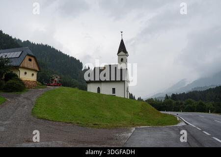 Piccola chiesa bianca tradizionale in piedi su una collina verde vicino ad una strada di montagna sotto un cielo coperto . Kapelle Maria Hilf (Pirkach-Kapelle) in Austria. Foto Stock