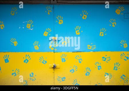 Una porta di garage in metallo dipinta con il blu e il giallo della bandiera Ucraina. La superficie è ricoperta da impronte di mani gialle e blu a contrasto. Foto Stock