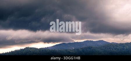 Nuvole di tempesta scure che si formano sopra le colline boscose di montagna, creando un paesaggio naturale drammatico e lunare. Foto Stock