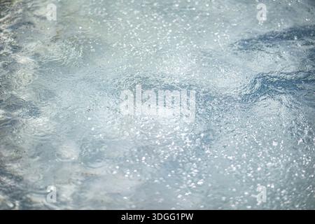 Primo piano di una superficie d'acqua azzurra con numerosi schizzi e increspature, che riflettono la luce e creano punti brillanti. Foto Stock