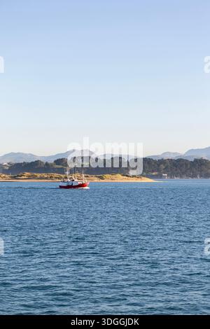 Una barca da pesca rossa e bianca che naviga nella baia di Santander, in Spagna, in una giornata di sole. Un concetto dell'industria della pesca e del lavoro marittimo tradizionale. Foto Stock