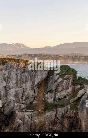 Una vista panoramica delle scogliere rocciose sulla penisola di Magdalena a Santander, in Spagna, con la baia e le montagne nebbiose sullo sfondo al tramonto. Foto Stock