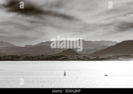Una fotografia in bianco e nero di un motoscafo veloce sulla baia di Santander, lasciando una suggestiva scia sulle acque scintillanti con le montagne sullo sfondo Foto Stock