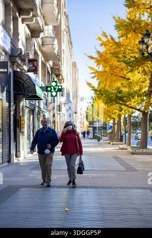 Santander, Spagna – 20 novembre 2021: Una coppia cammina lungo Calle Calvo Sotelo in una soleggiata giornata autunnale. Un segno di farmacia sullo sfondo mostra una temperatura Foto Stock
