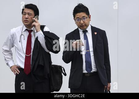 Due uomini d'affari in tuta, uno al telefono, l'altro con uno smartphone, Tokyo, Minato, Giappone Foto Stock