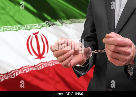 Un uomo con una tuta d'affari sta in manette contro la bandiera dell'Iran Foto Stock
