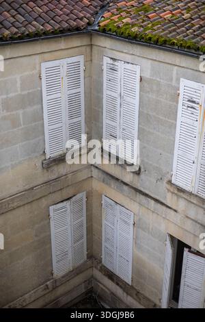 La facciata intemprata di un vecchio edificio in pietra con persiane chiuse in legno bianco sbucciante. Un concetto di storia architettonica, abbandono e bea Foto Stock