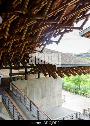 Guardando verso l'alto una struttura del tetto in legno altamente complessa sostenuta da pilastri in cemento grezzo. Le intricate travi in legno a incastro sono caratterizzate da archi avanzati Foto Stock