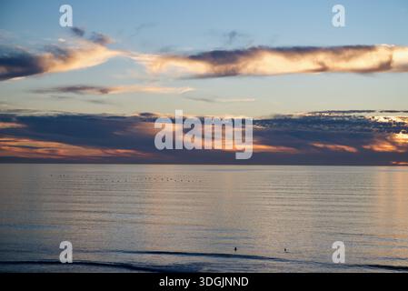 Vista mozzafiato dell'oceano al tramonto con vivaci sfumature di arancione e blu che si riflettono sull'acqua. Il cielo sereno incontra l'orizzonte infinito. Foto Stock