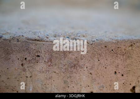 Immagine ravvicinata di una superficie in cemento ruvido e ruvido con piccoli fori e imperfezioni, che mostra l'usura naturale e gli agenti atmosferici del materiale. Foto Stock