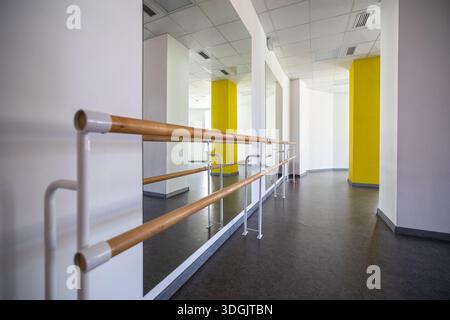 Un luminoso studio di danza interno con barrette di balletto in legno, pareti a specchio e colonne gialle strutturali, fornendo uno spazio di pratica aperto. Foto Stock