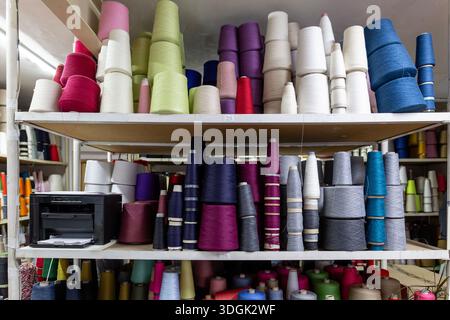 Gli scaffali di un magazzino di produzione di maglieria sono pieni di coni colorati e bobine di filati. Questo stoccaggio mostra le materie prime per la lavorazione a maglia, incl Foto Stock